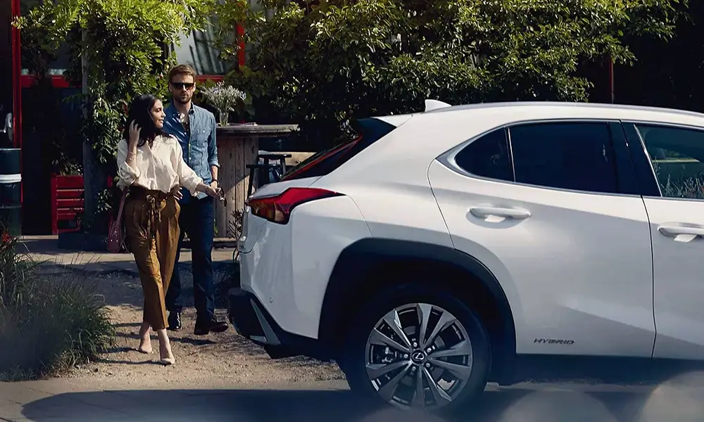 Elegáns pár egy fehér Lexus hibrid autó mellett.
